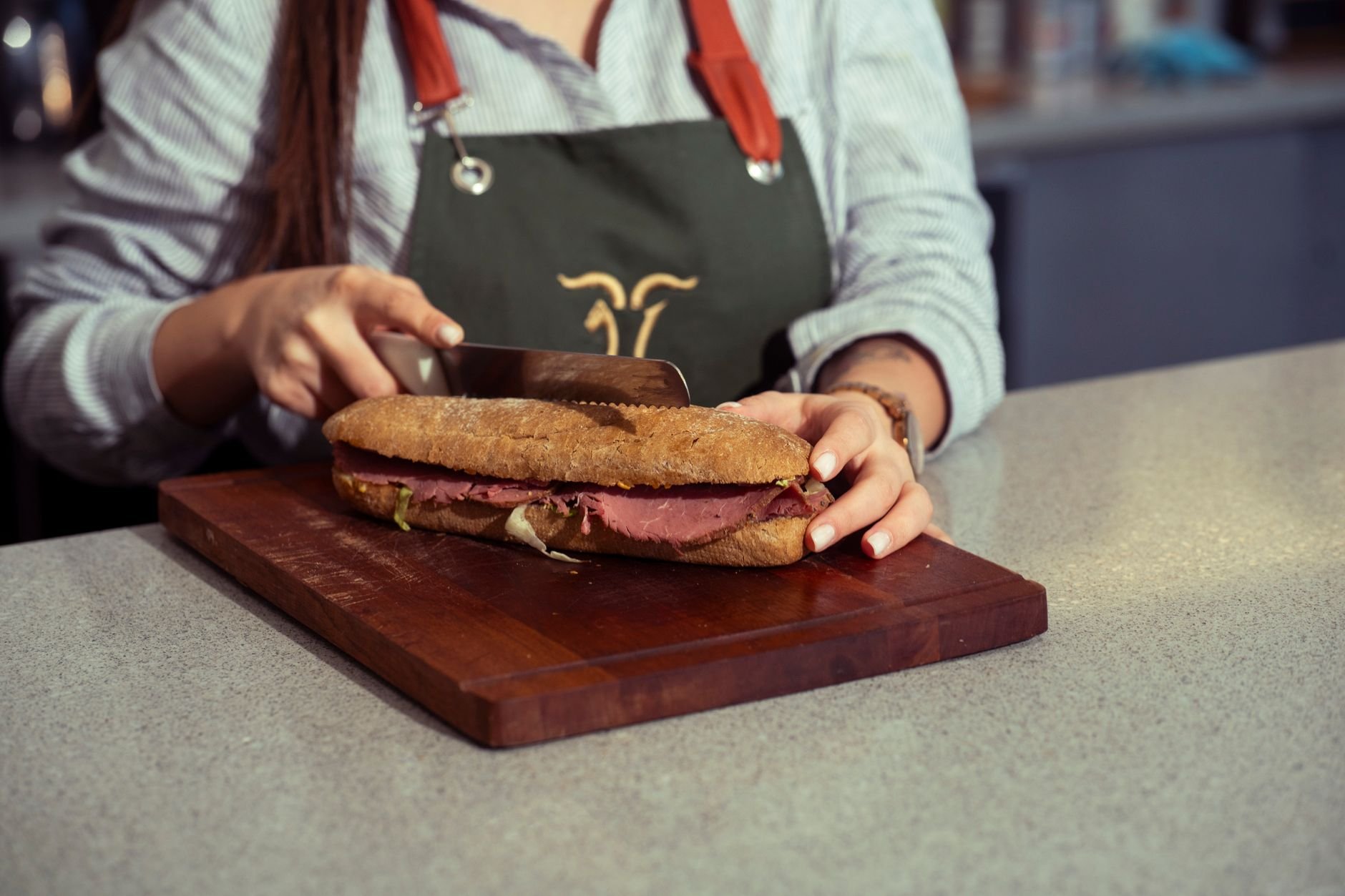 Close-up of a chef slicing a fresh gourmet sandwich on a wooden cutting board indoors.